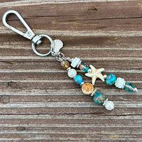 Beach-Themed Charm
Handmade charm with a coastal design, featuring Czech beads, gemstones, and a seashell charm perfect to clip to a purse.